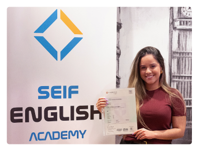 Estudiante sonriente en las modernas instalaciones de la academia en Gran Vía 50, mirando a cámara y sosteniendo su certificado que demuestra haber aprobado el examen Cambridge First (FCE).